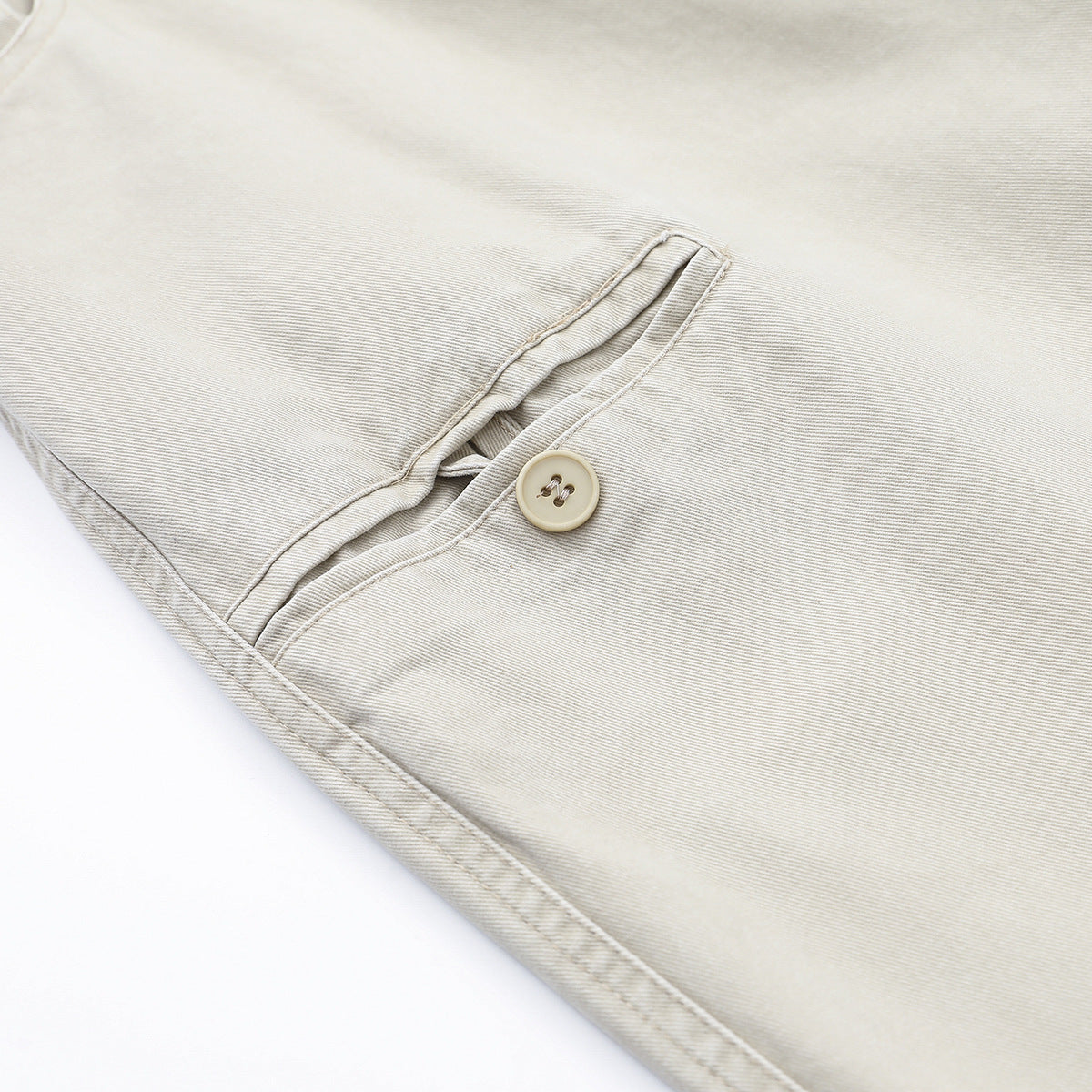 Close-up of light beige trousers showing the button closure, fly, and surrounding stitching.
