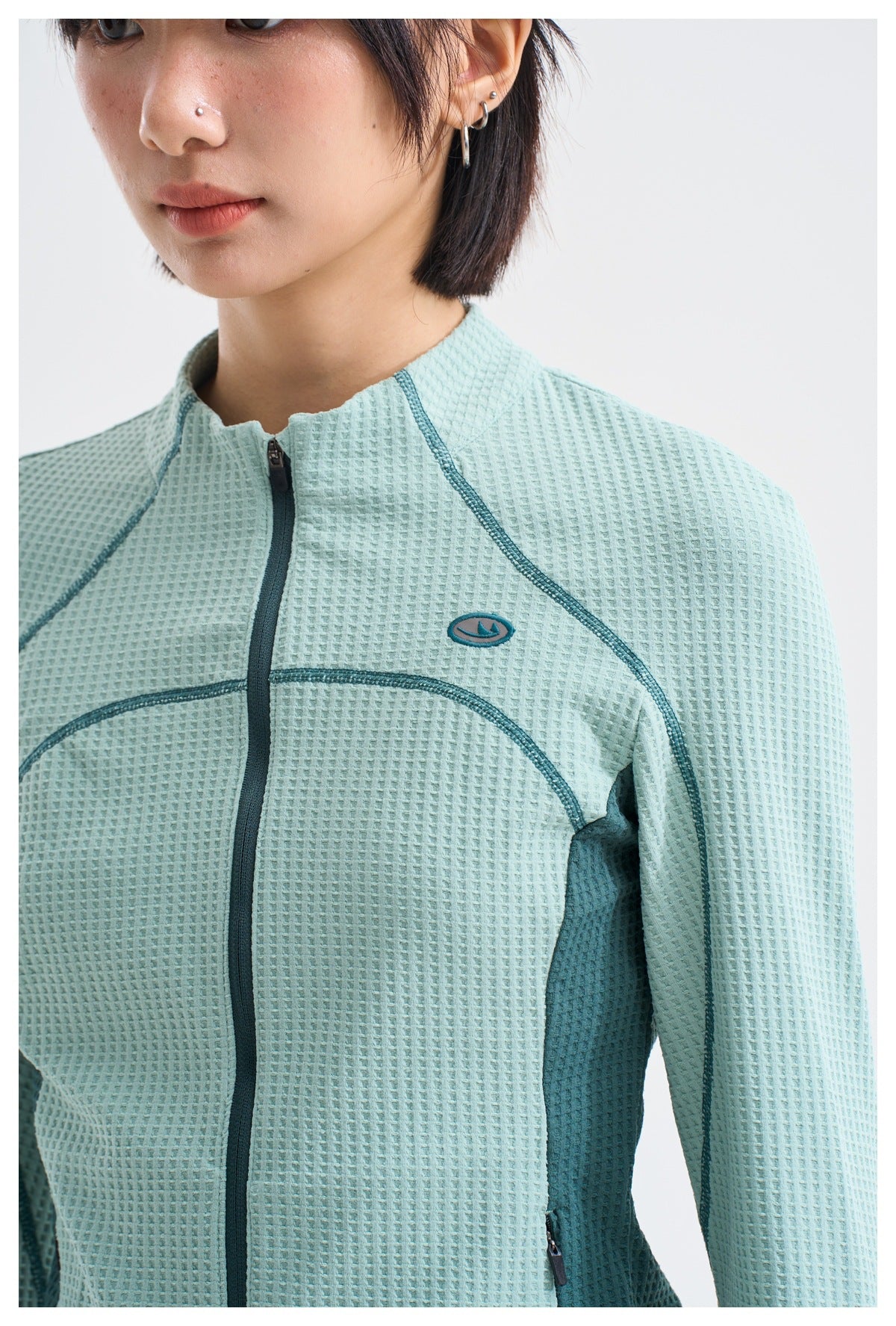 Close-up of a mint-green textured jacket showing its dark teal zipper, contrast stitching and side panels.