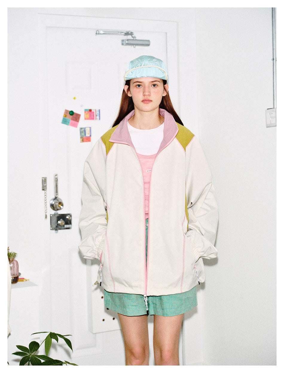 Model wearing the beige jacket zipped open with hands in pockets, over a pink top and green checked shorts