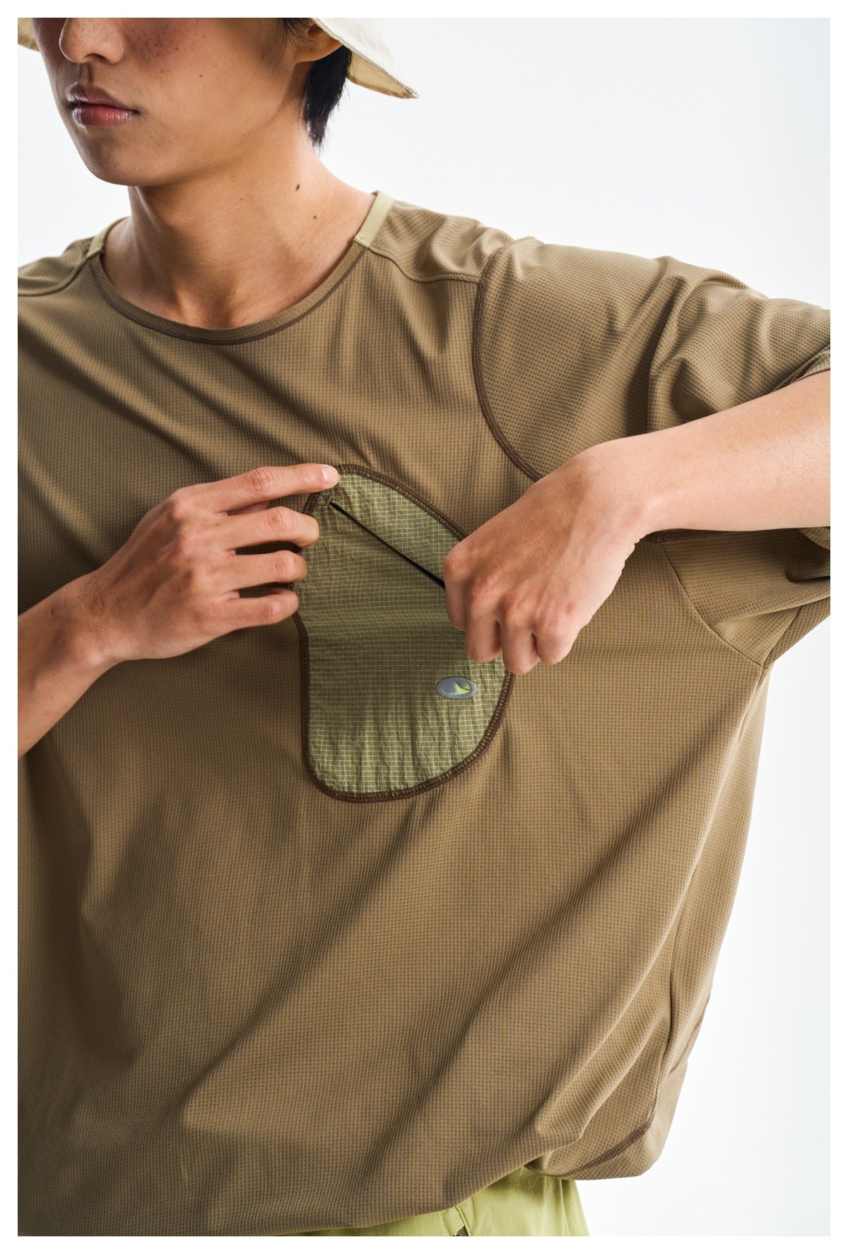 Close-up of a brown T-shirt's contrasting chest pocket as the model opens its zipper.