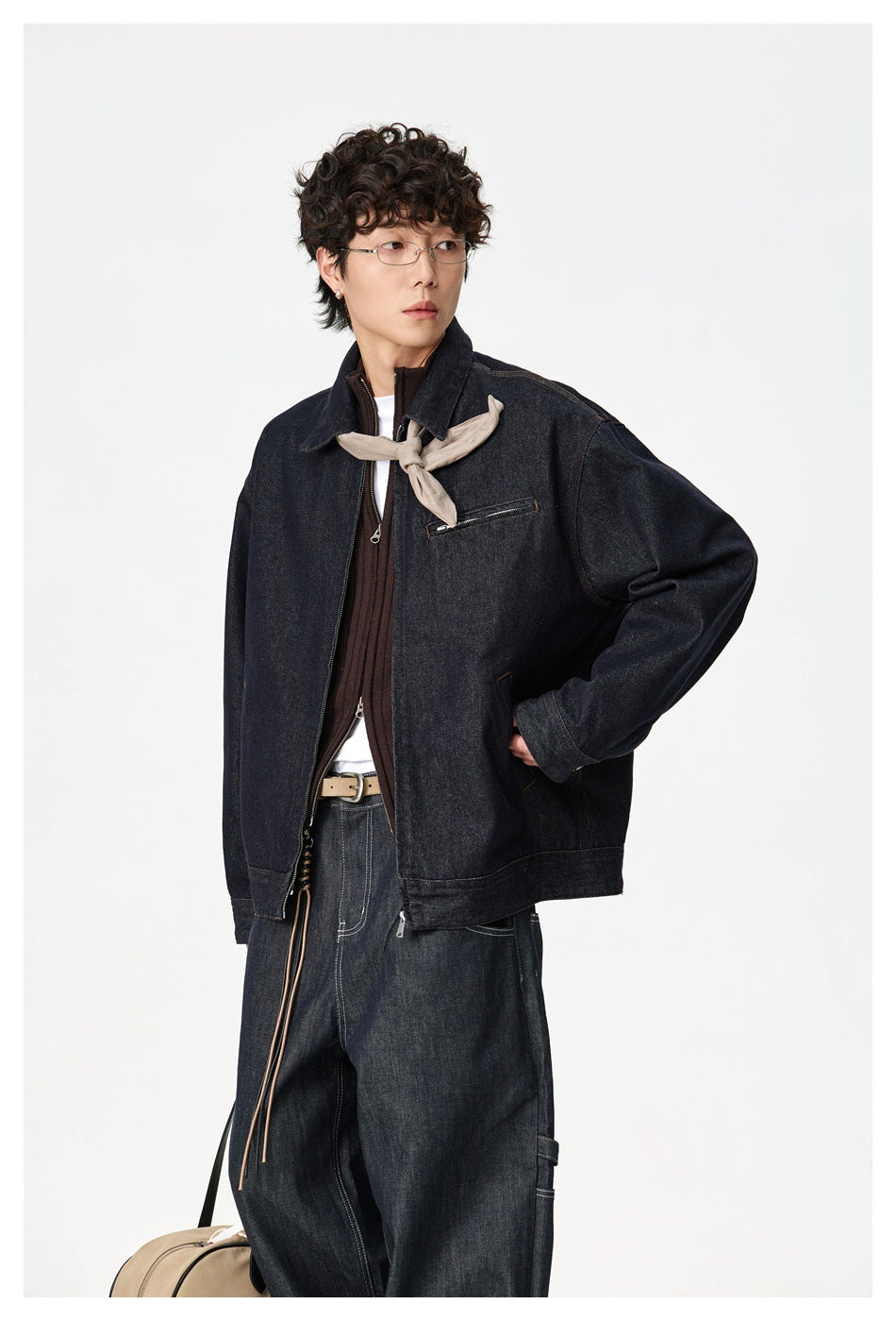 Model wearing an open dark indigo denim jacket with a zip chest pocket and a light scarf at the neck.