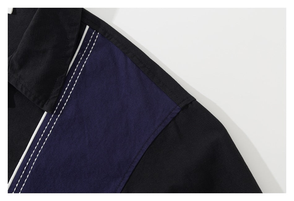 Close-up of a black shirt shoulder with a navy color-block panel, white piping and double stitching.