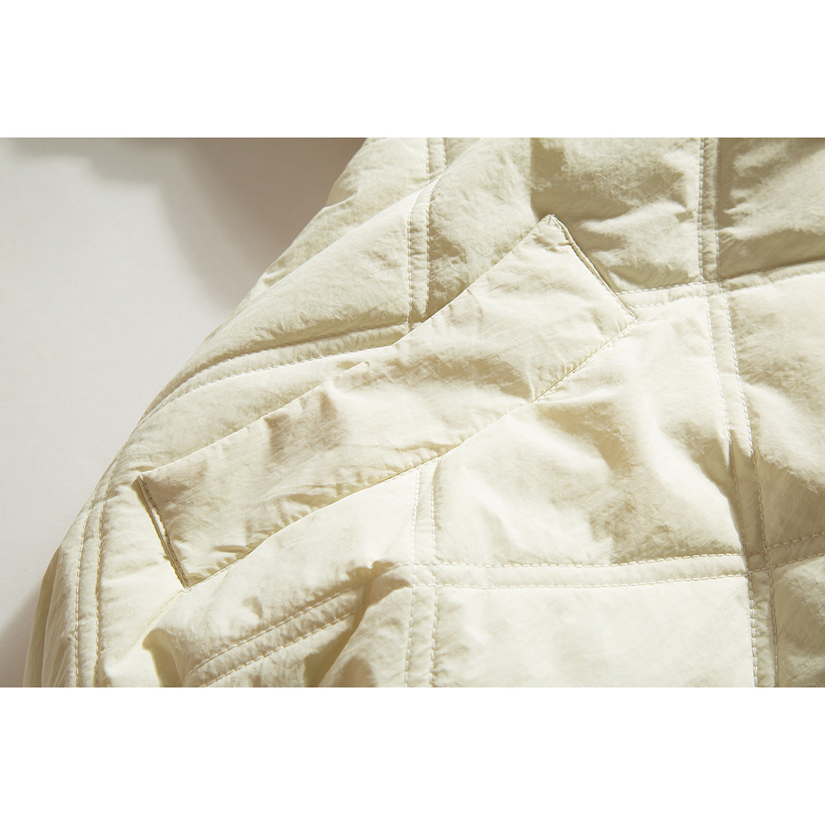 Close-up of ivory jacket quilting, stitched seams, and a flap pocket.