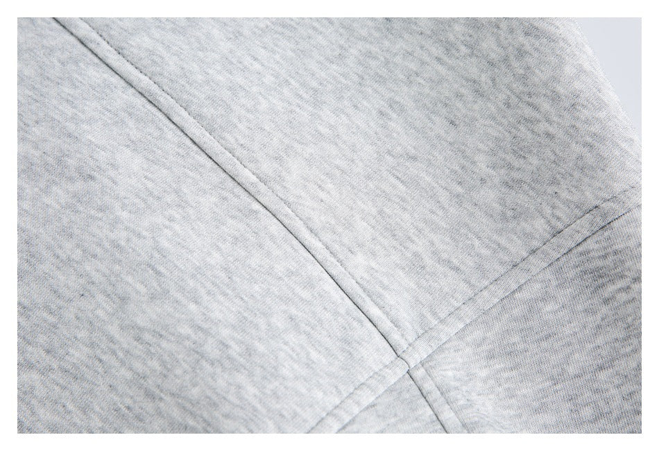 Close-up of light gray heather garment fabric showing intersecting stitched seams.