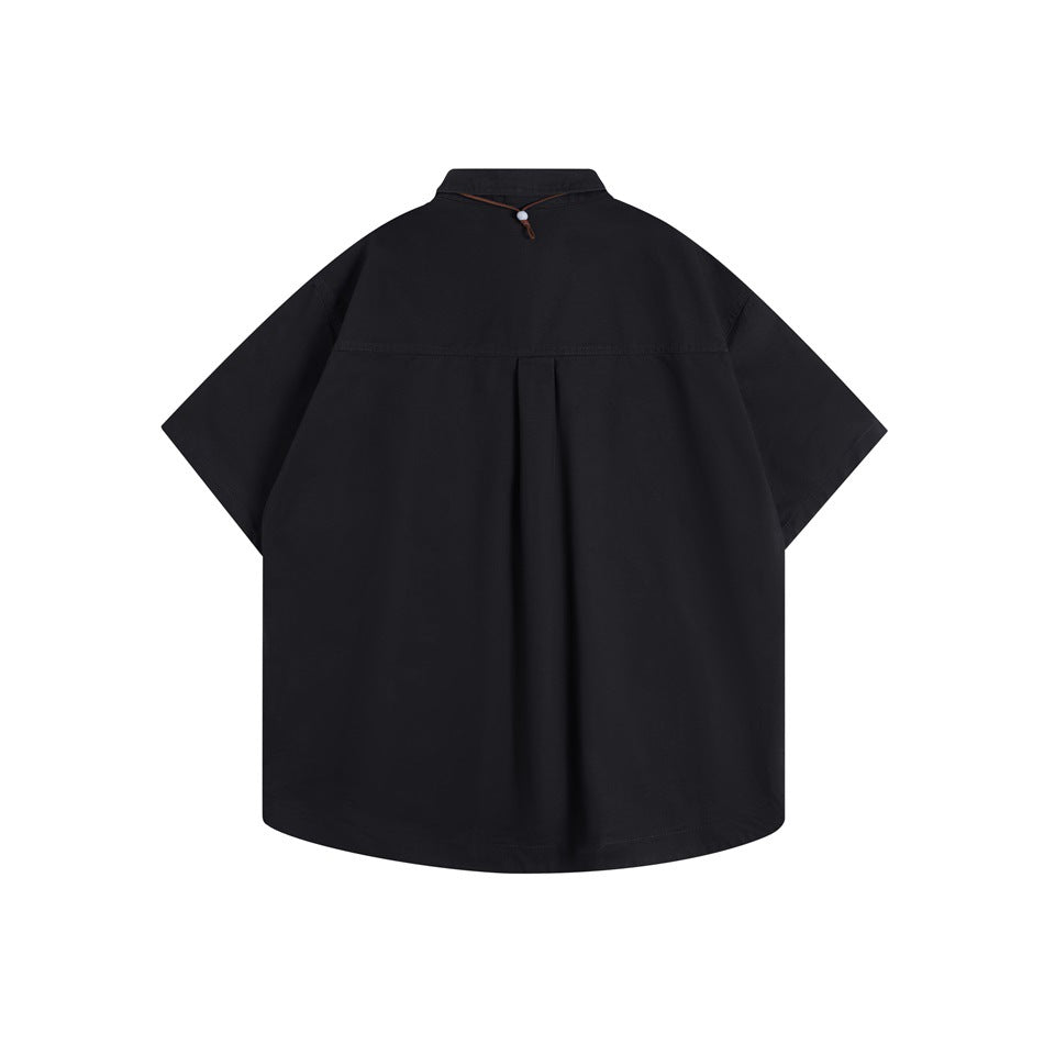 Back view of a black short-sleeve button-up shirt with a yoke seam, center pleat, and brown cord detail at the collar.