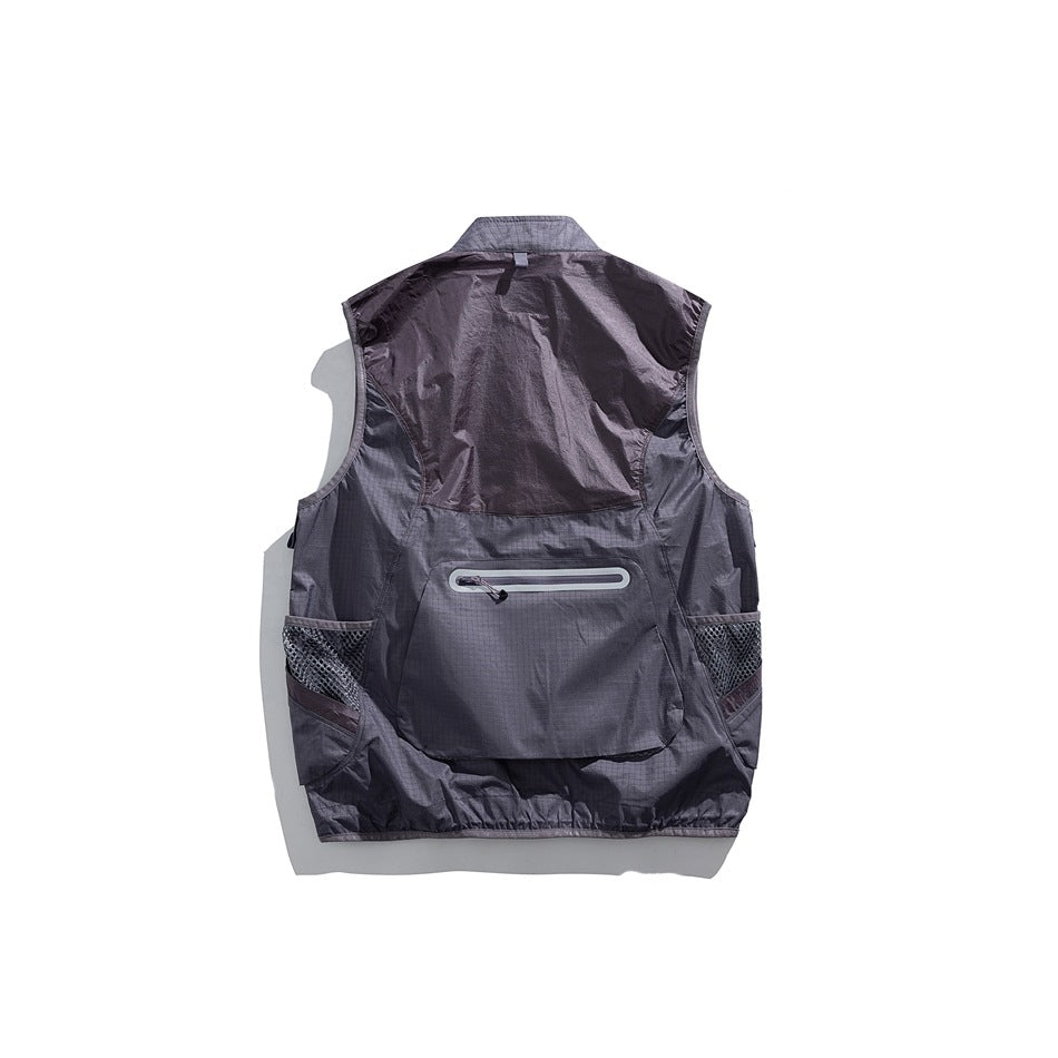 Back view of a dark charcoal utility vest with mesh side pockets and a horizontal zip pocket.