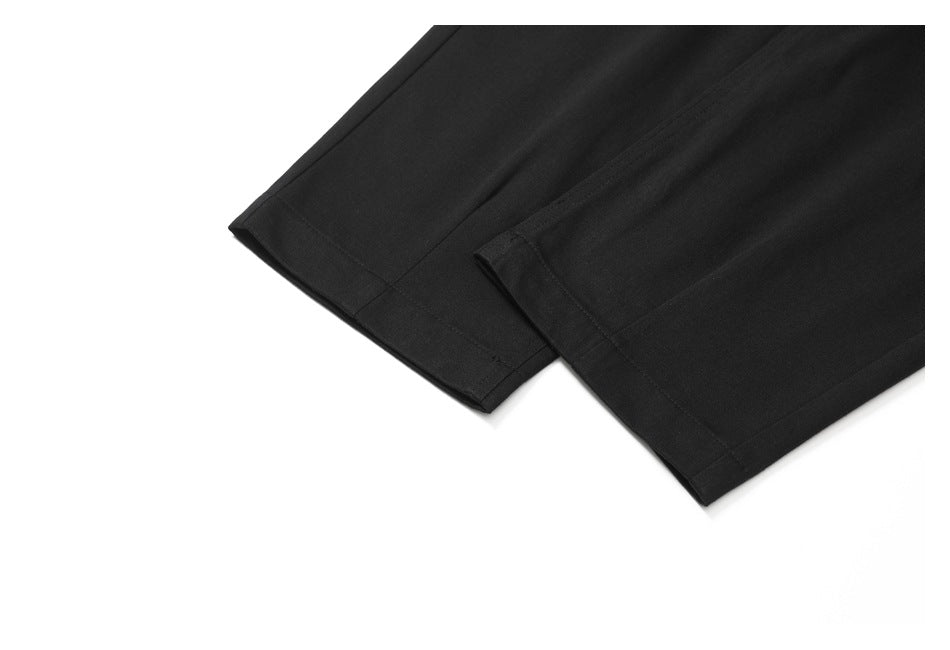 Close-up of the hems of black trouser legs against a white background.