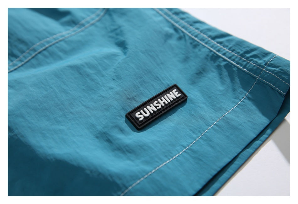 Close-up of a black SUNSHINE patch and contrast stitching on turquoise shorts.