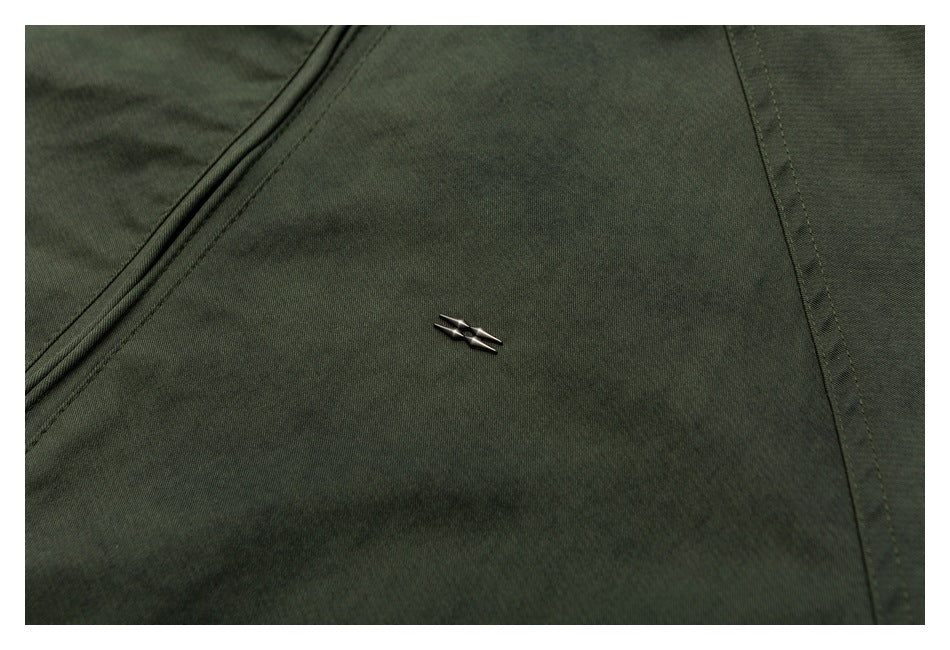 Close-up of a small metallic emblem on dark olive fabric beside a stitched seam.