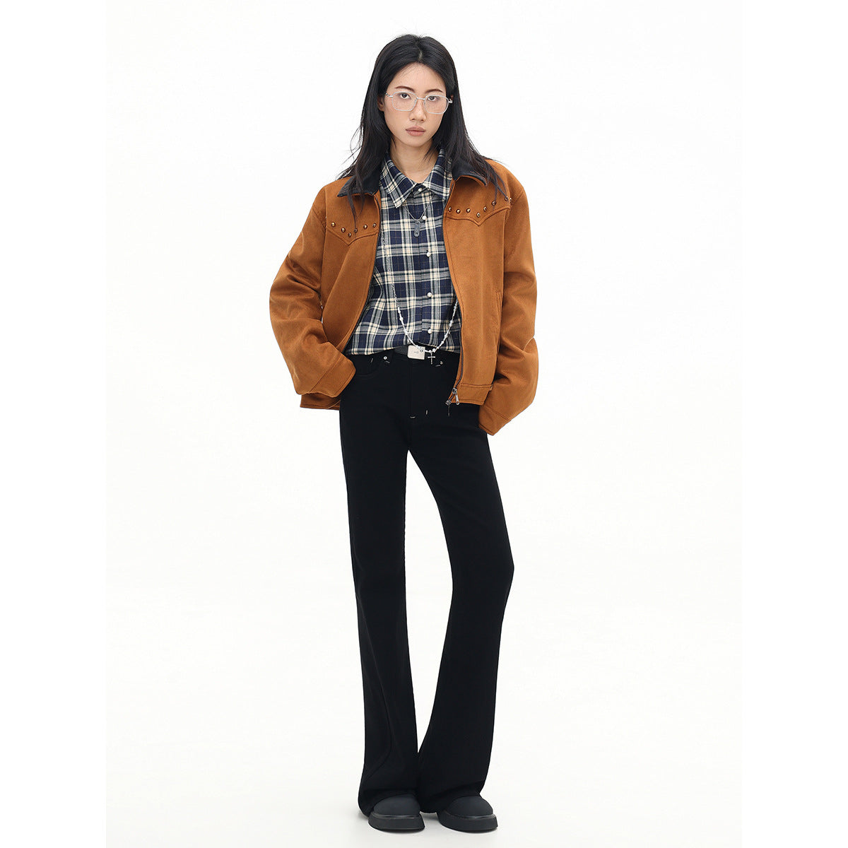 Full-length model wearing a rust-brown studded jacket over a navy plaid shirt, with black flared trousers.