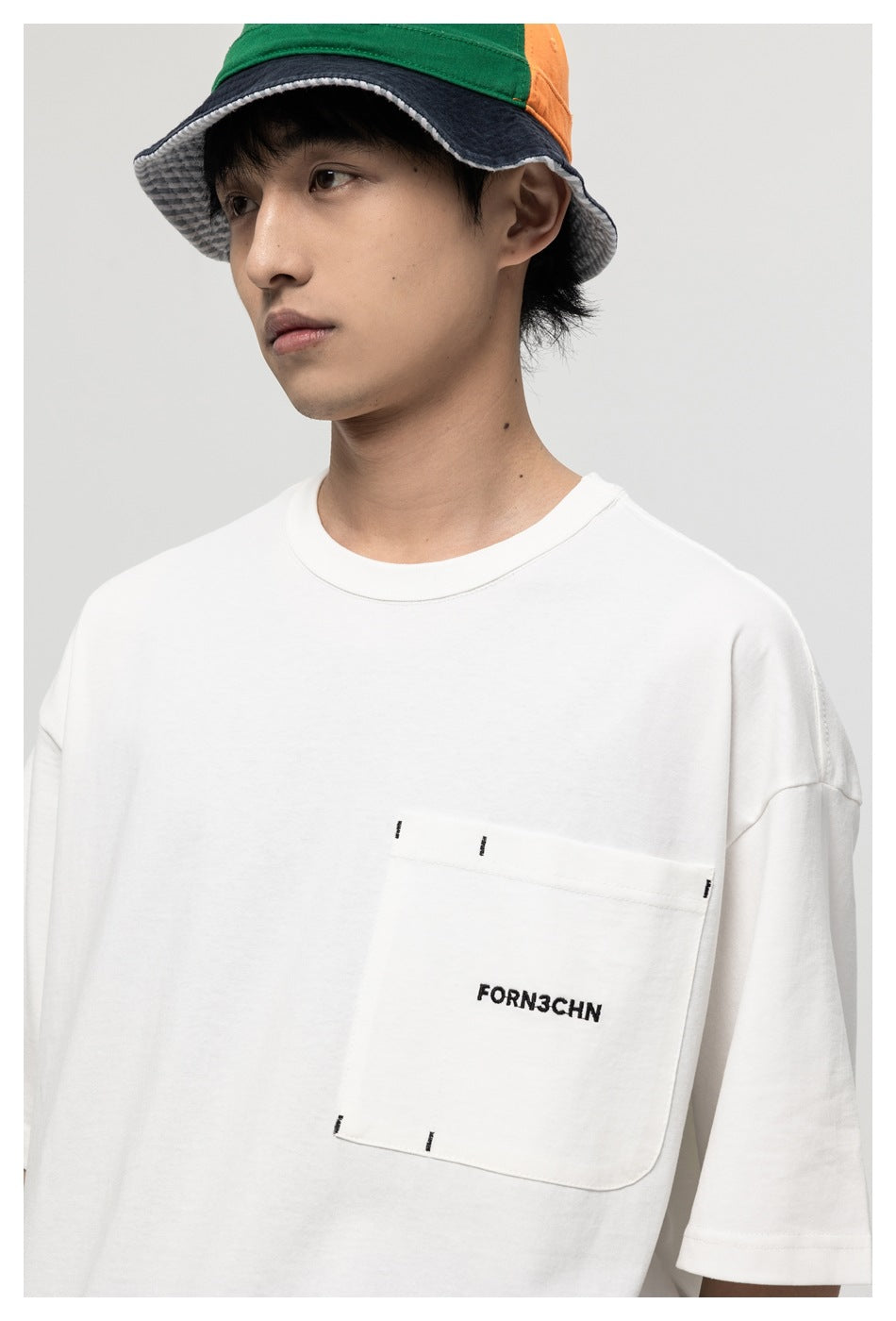 Close-up of a model wearing a white oversized T-shirt with a stitched chest pocket and small black lettering.