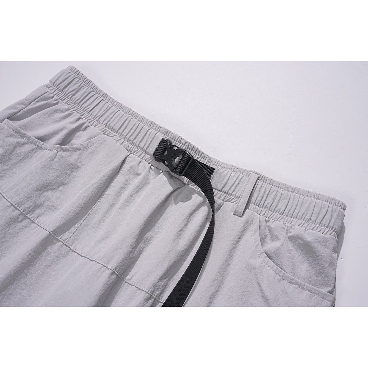 Close-up of pale gray skirt waistband with elastic gathering, black buckle belt, and curved front pocket.