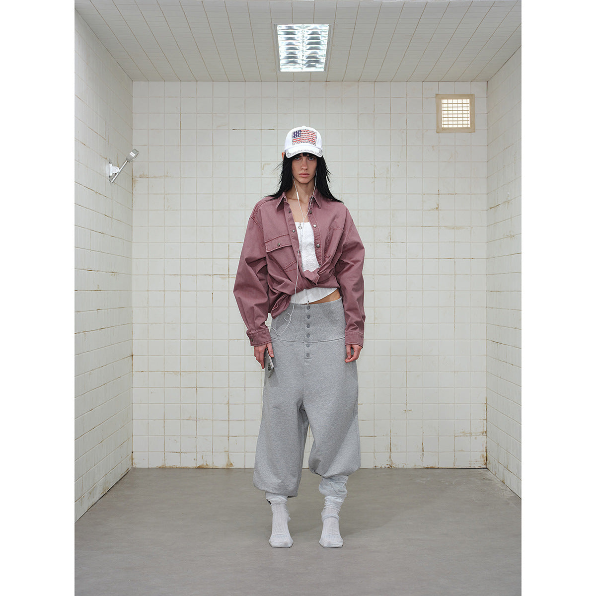 Full-length front view of a model wearing a dusty mauve shirt, gray loose pants, and a white cap.