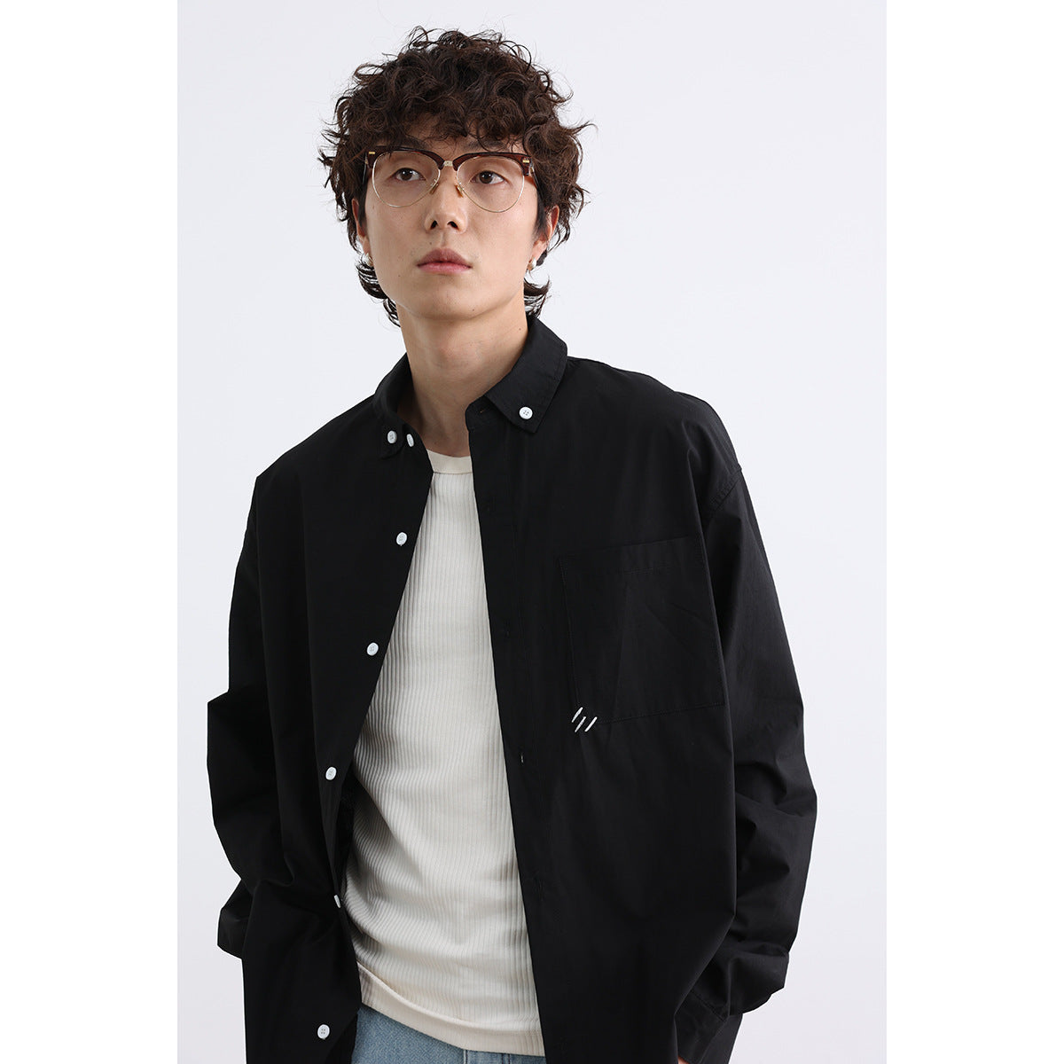 Close view of a model wearing a black button-down shirt with a chest pocket over a white top.
