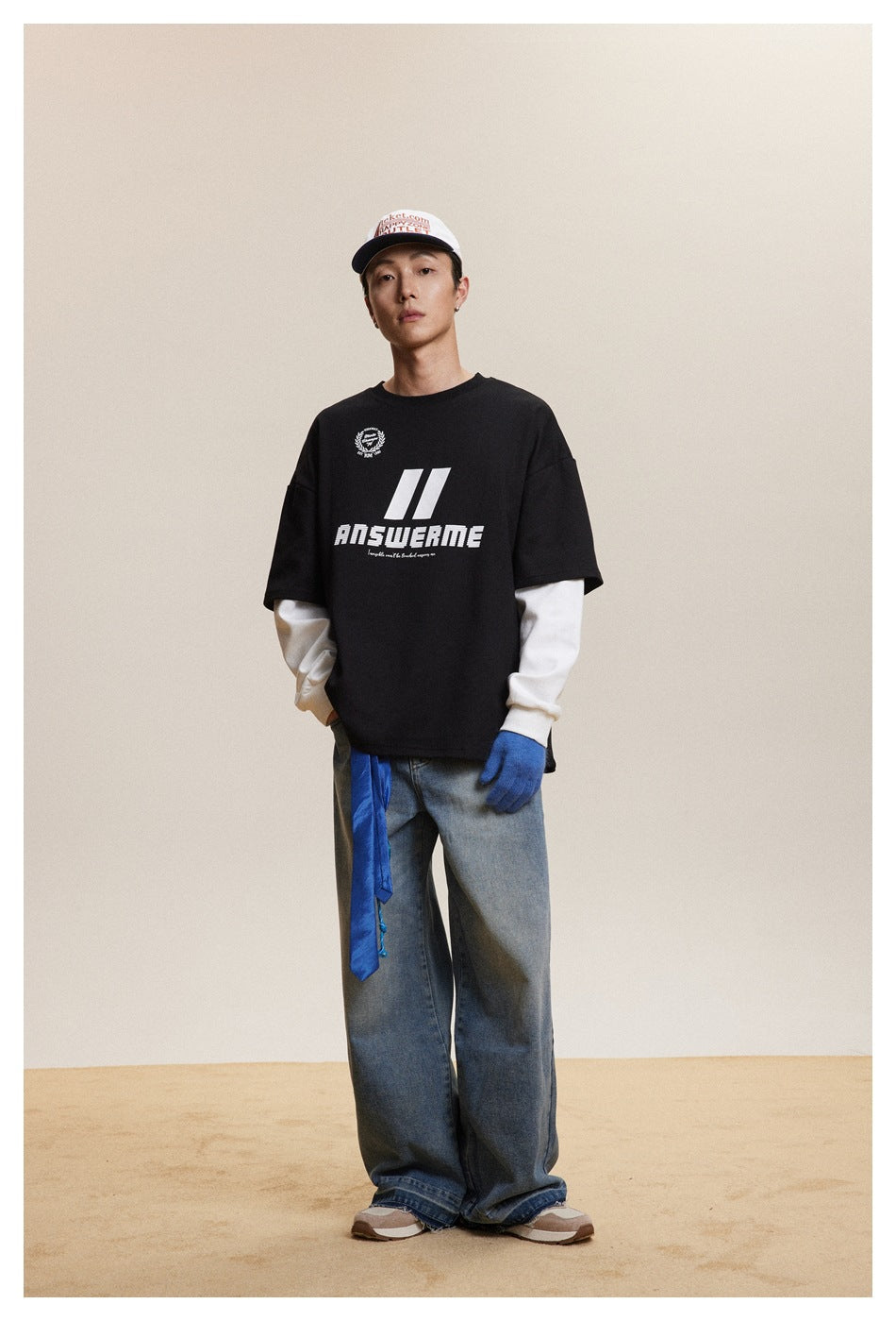 Model in black layered-look top with white sleeves, ANSWERME graphic, cap and wide-leg jeans, front view