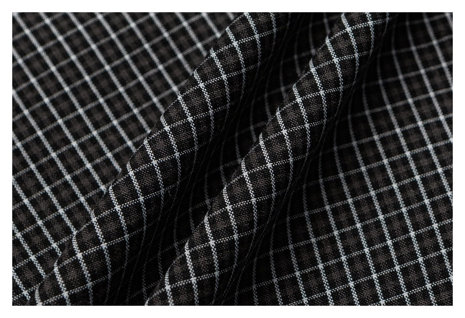 Macro view of folded black fabric with a fine white grid pattern and visible stitching along the folds.