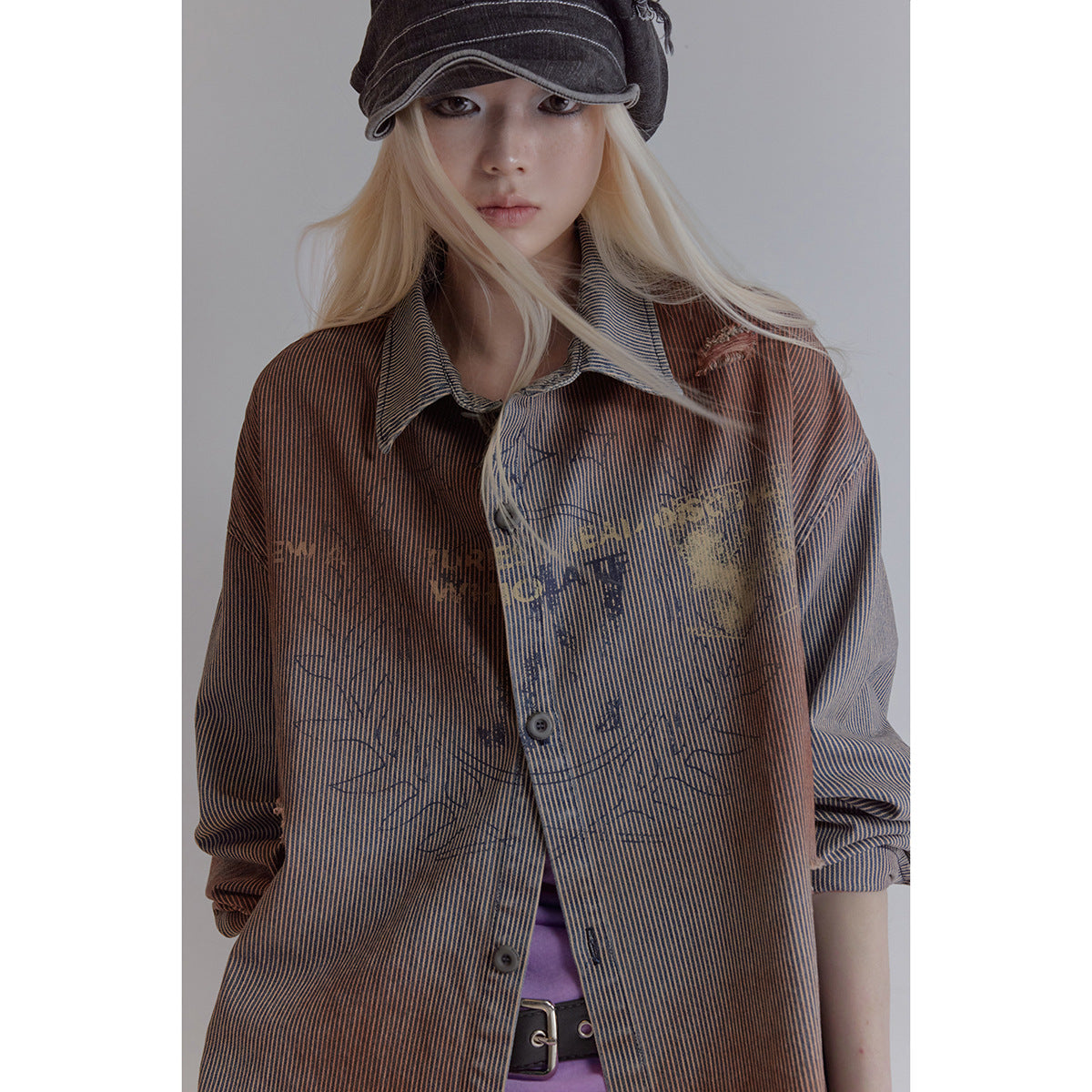 Model wearing a distressed copper and navy pinstriped button-up jacket with a black cap.