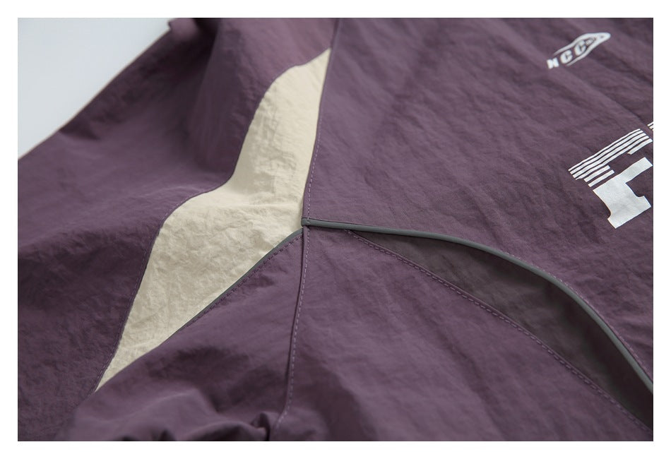 Close-up of plum garment panels with a cream inset, gray piping, and partial white lettering.
