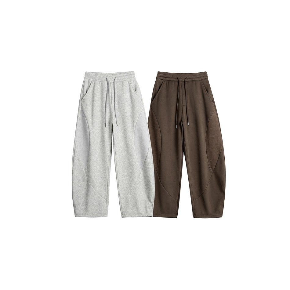 Front view of two loose-fit sweatpants, one light gray and one dark brown, with drawstrings and curved seams.