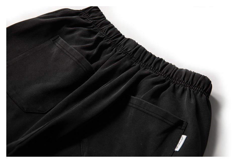 Close-up of black pants showing an elastic waistband, two rear patch pockets, and a small white woven tag.