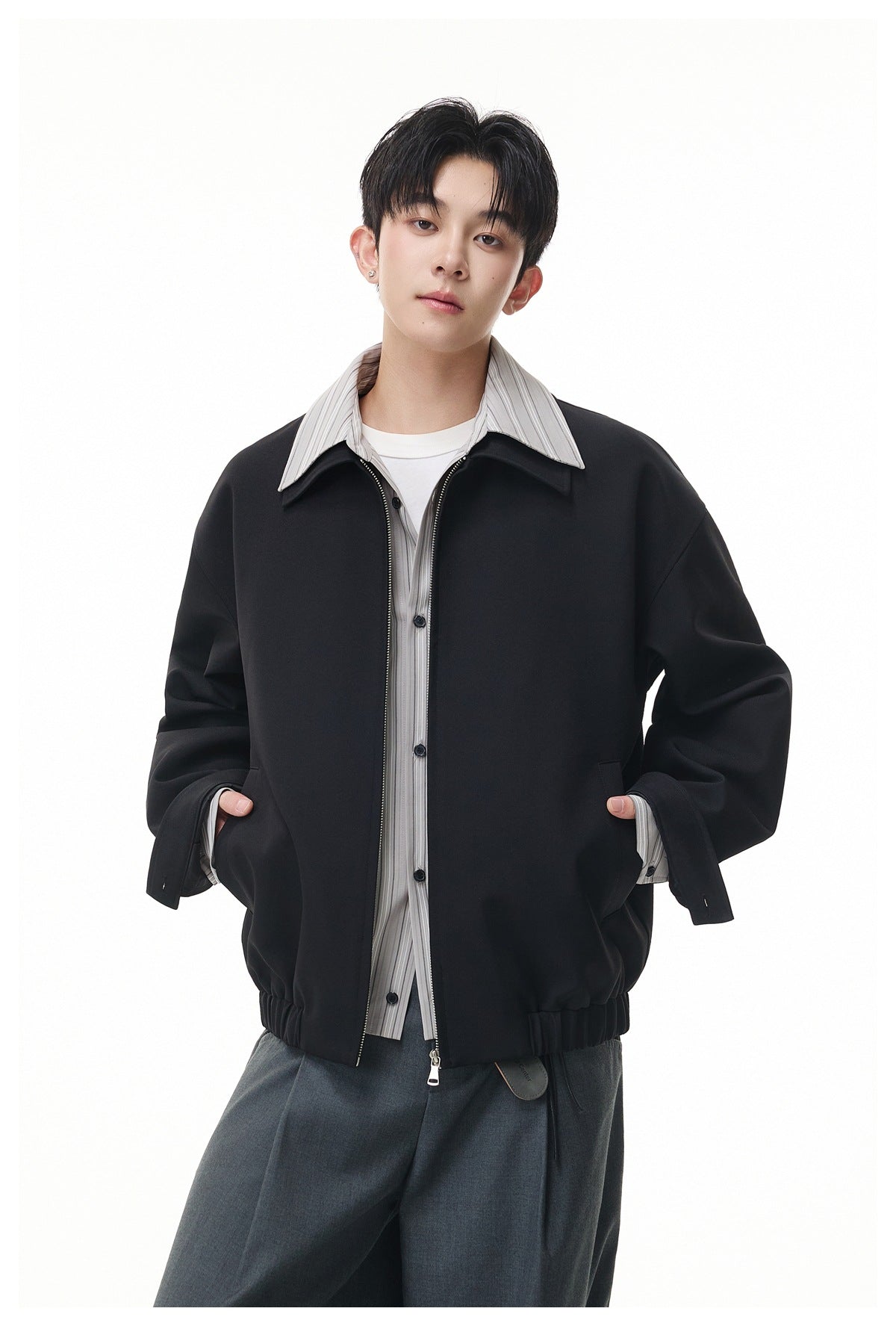 Model wearing a black oversized zip jacket with a wide collar over a gray striped shirt.