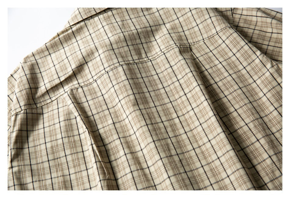 Close-up of beige plaid shirt fabric showing a curved seam and folded construction.