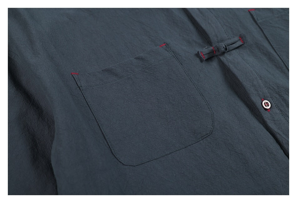 Close-up of a charcoal-blue garment showing a patch pocket, loop closure and button with red accents.