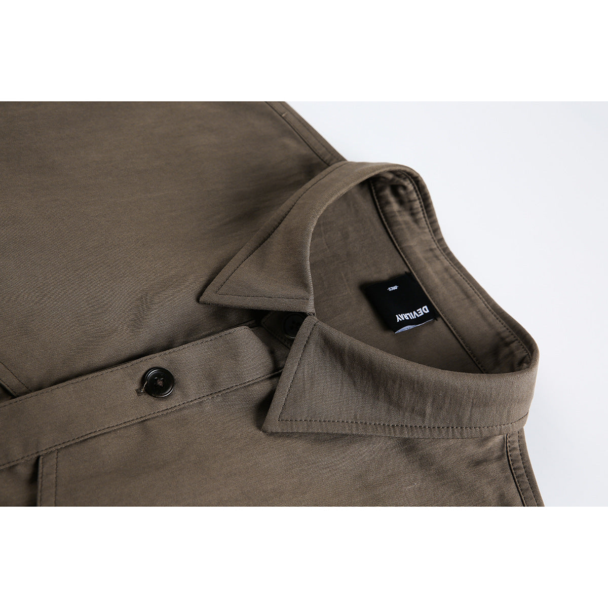 Close-up of a brown collared shirt showing the collar, black buttons, stitching, and a black neck label.