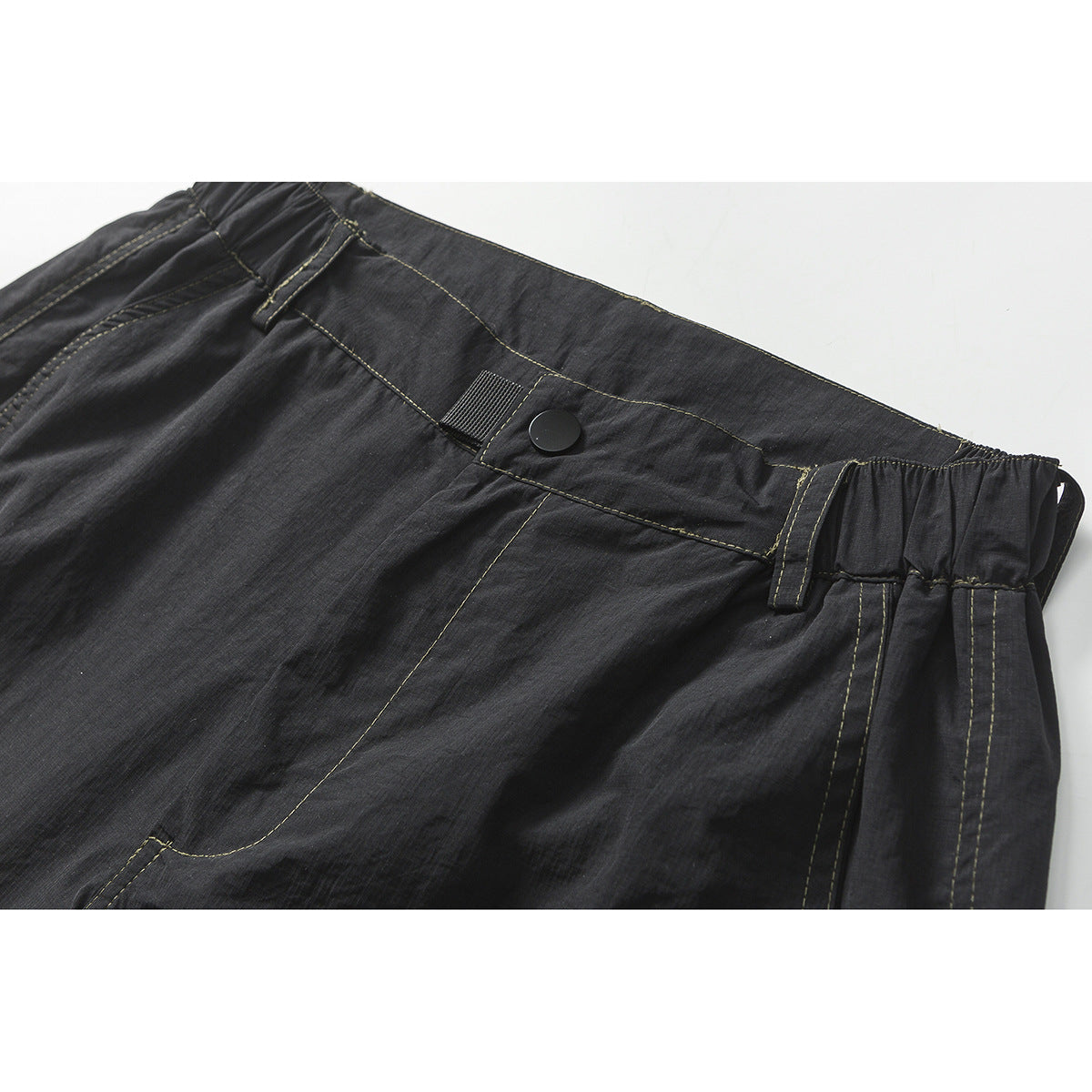 Close-up of charcoal shorts showing the buttoned waistband, belt loops, elastic side panel, and contrast stitching.