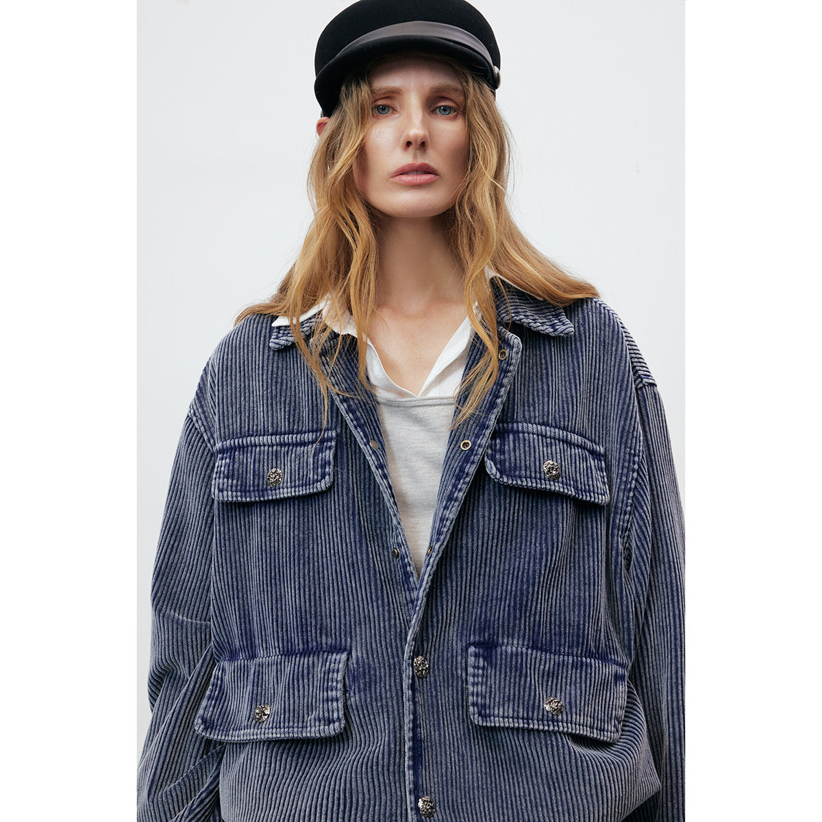 Close view of a model wearing a blue ribbed jacket with a pointed collar and four buttoned flap pockets.