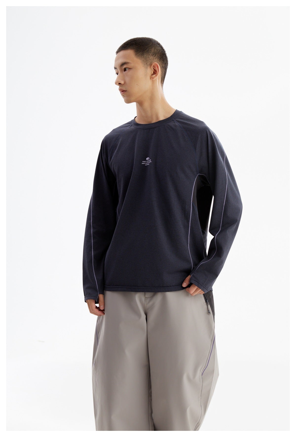 Model wearing a dark navy long-sleeve crewneck with lilac piping and a small white chest print.