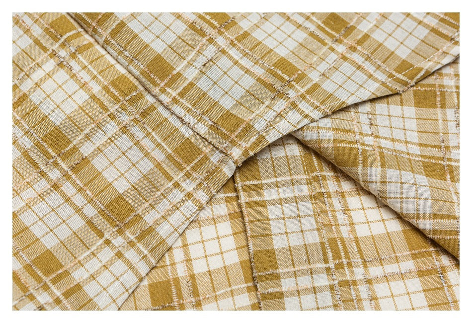 Close-up of layered mustard and cream plaid fabric showing intersecting seams and stitching.