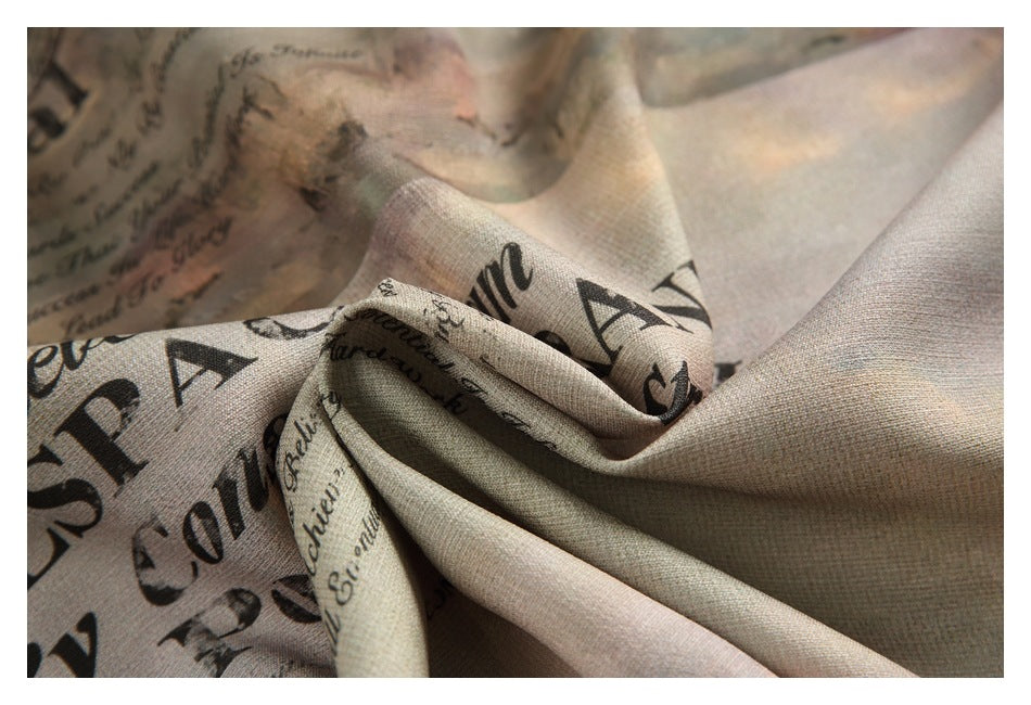 Draped close-up of beige printed shirt fabric with black English lettering and visible woven texture.