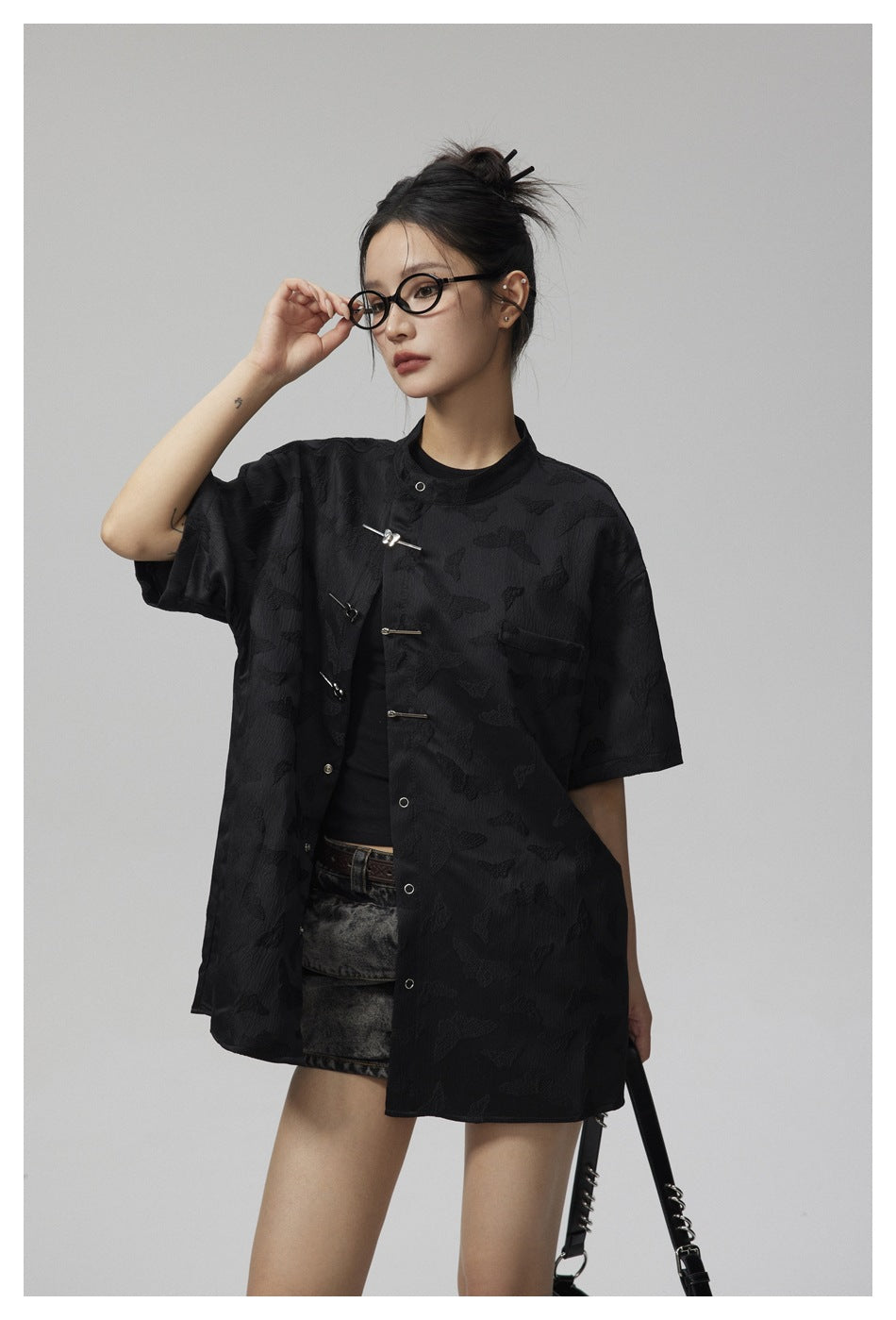Model wearing a black short-sleeve stand-collar jacket with frog closures and a subtle raised butterfly pattern.