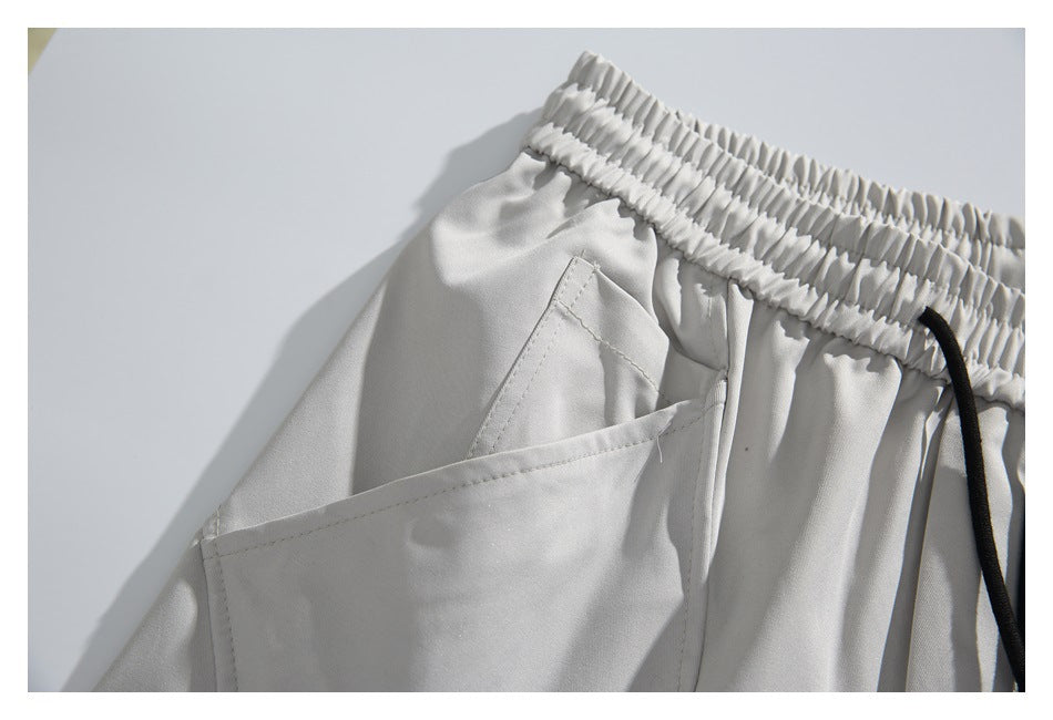 Close-up of a side pocket, gathered waistband, and black drawstring on light gray shorts.