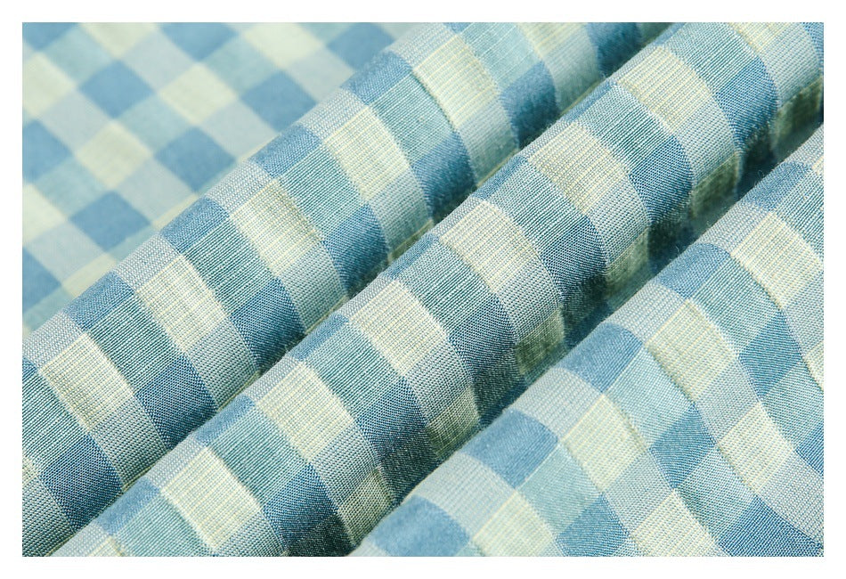 Macro view of blue and pale yellow checked fabric arranged in soft folds, showing its woven texture.