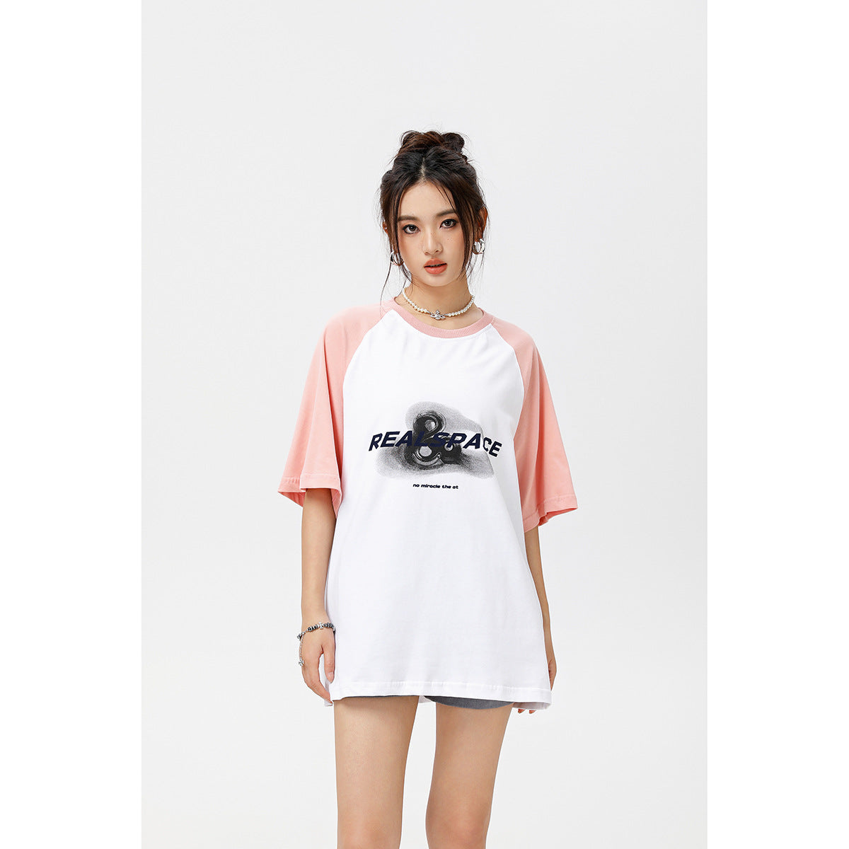 Front view of a model wearing an oversized white T-shirt with pale pink raglan sleeves and a black chest graphic.