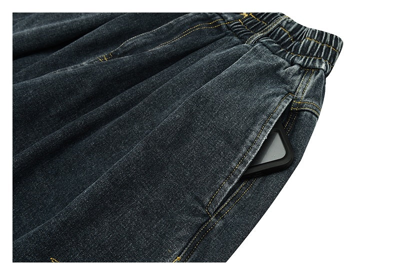 Close-up of a side pocket opening on dark denim pants, with a dark rectangular object partly visible inside.