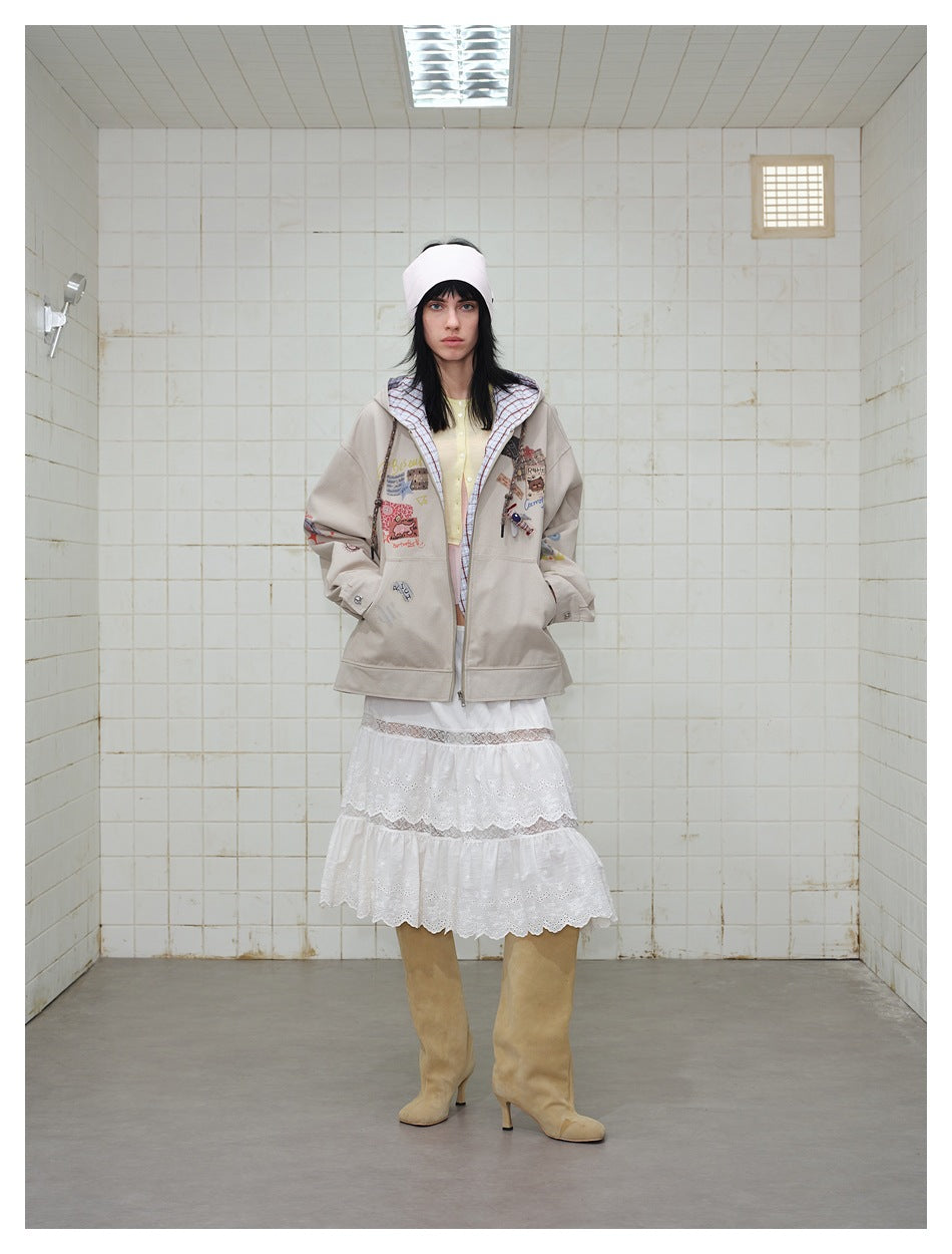 Model wearing a beige hooded jacket with colorful patches, shown from the front with a white lace skirt and tan boots.