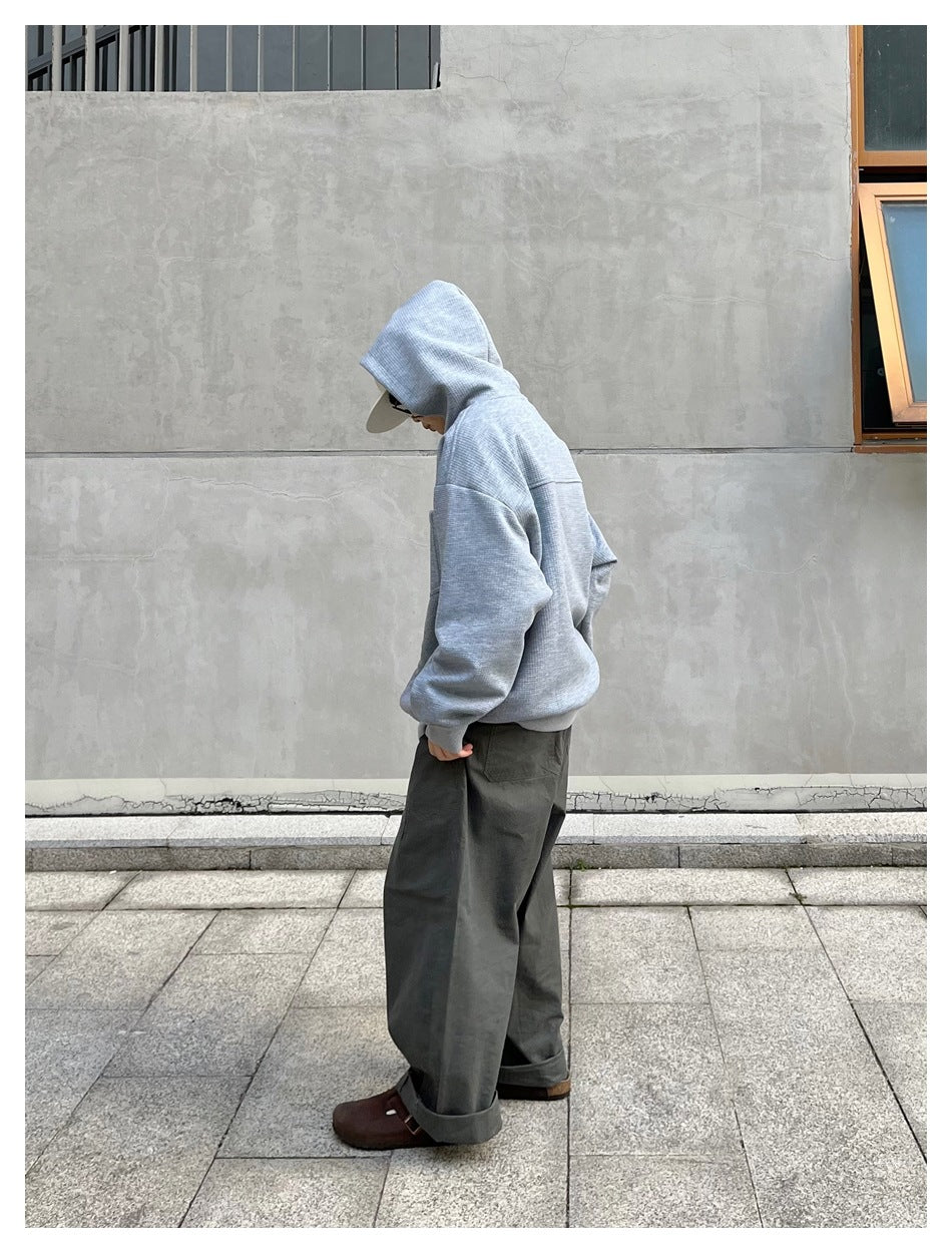 Person in gray zip-up hoodie with hood up, side view, with olive wide-leg pants and brown clogs