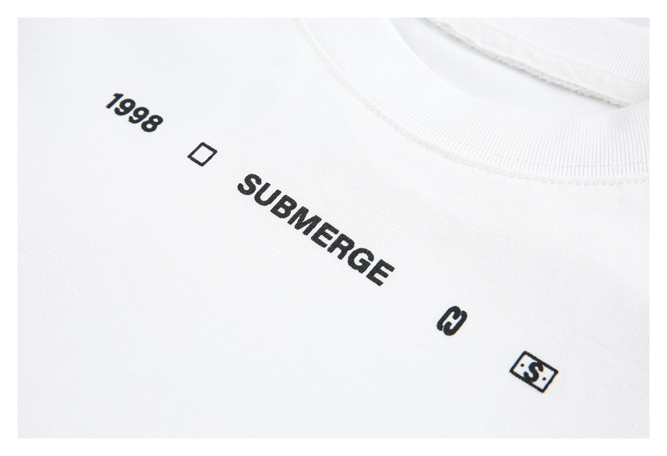 Close-up of black T-shirt chest print reading “1998” and “SUBMERGE” with small symbols on white fabric.