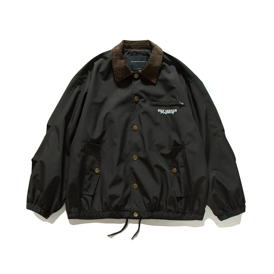 Black coach jacket with brown corduroy collar, snap buttons, zip chest pocket and flap pockets, flat lay front view