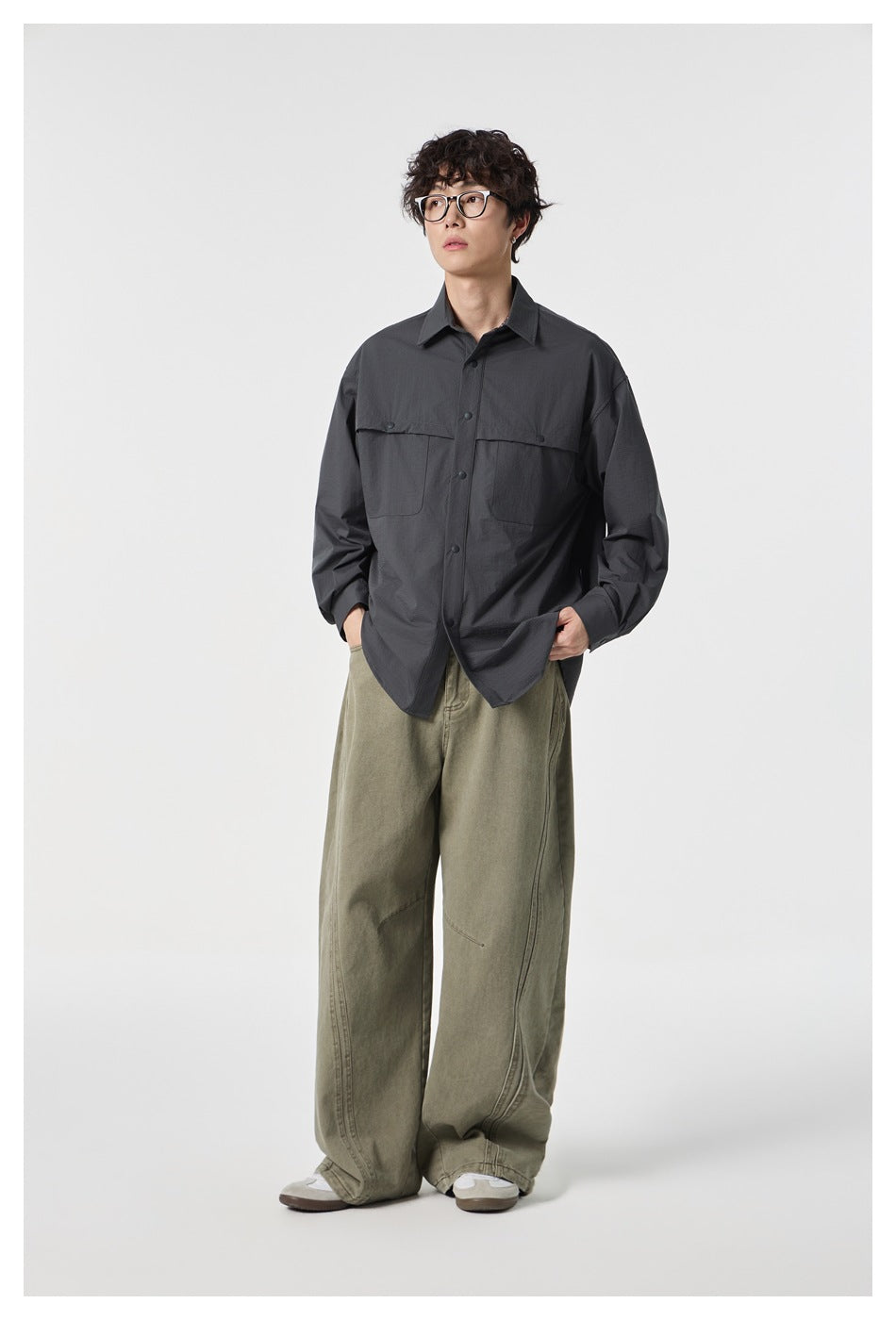 Model wearing dark gray pocketed shirt open-front styled with wide olive pants, one hand in pocket
