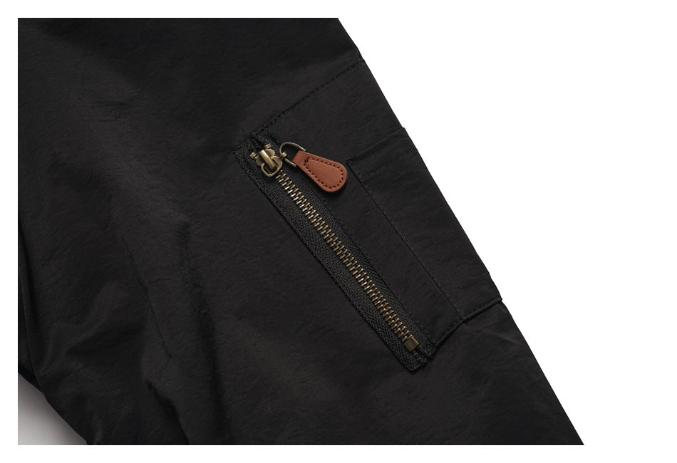 Close-up of a vertical brass-tone zip pocket with a brown pull tab on the black jacket sleeve.