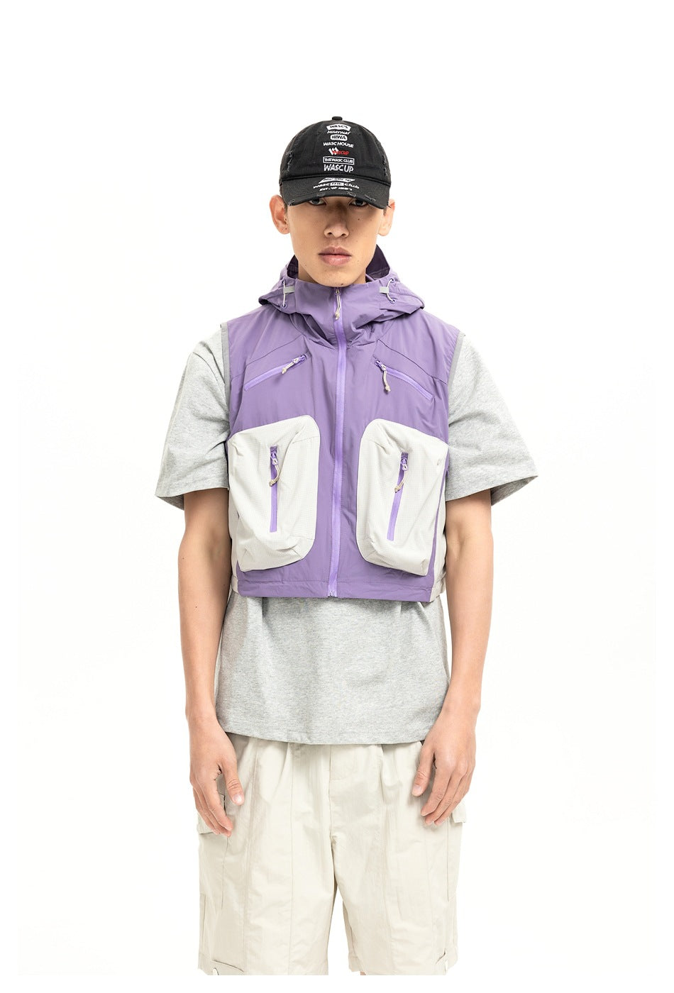 Model wearing a purple hooded cropped utility vest with large front pockets over a gray T-shirt, front view