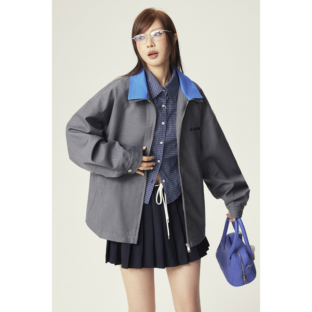 Close view of a model wearing an oversized gray jacket with a blue collar over a blue checked shirt.