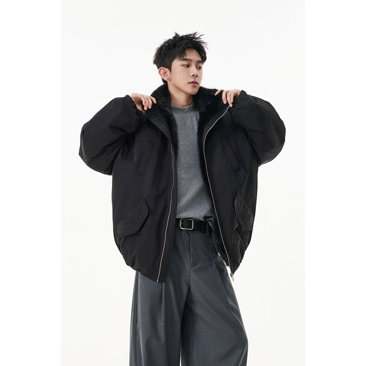 Model wearing an oversized black jacket with a black fur collar, open over a gray top.