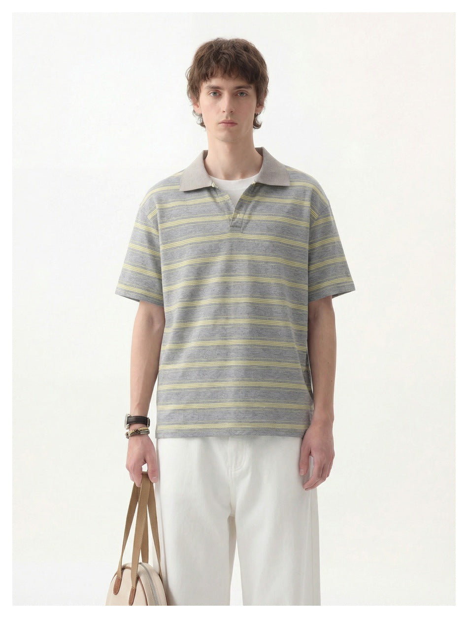 Man wearing a gray and yellow striped short-sleeve polo top with white pants, front view, holding a tote bag