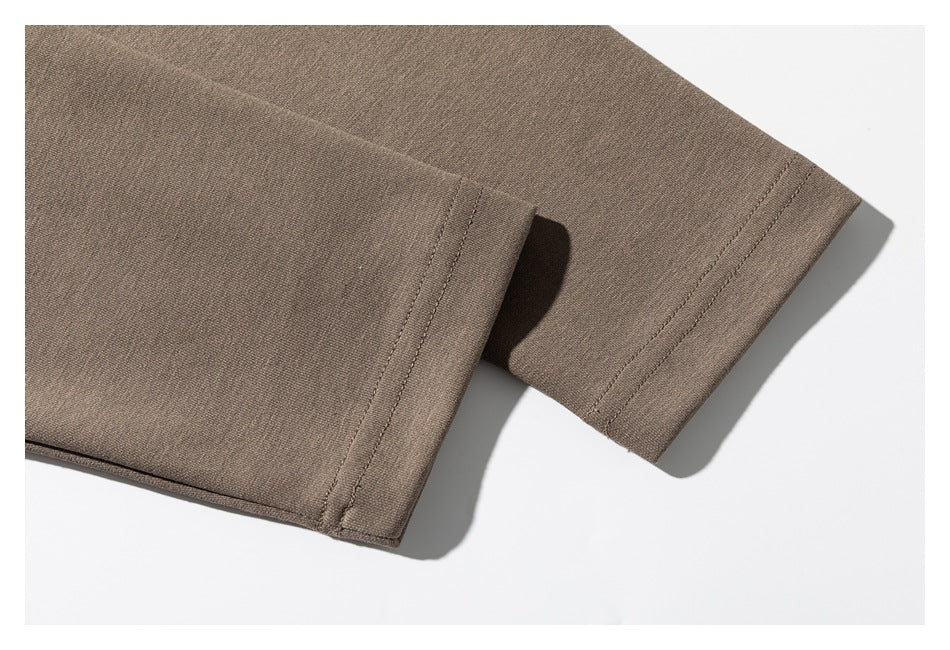 Close-up of a taupe garment showing a stitched hem and overlapping fabric edge.