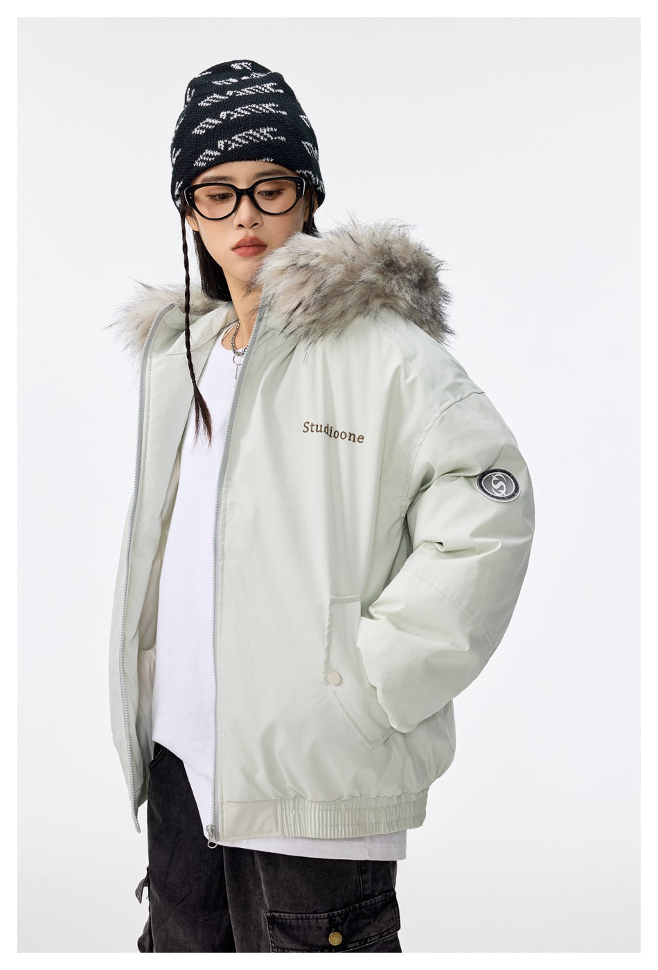 Model wearing a pale gray hooded jacket with light fur trim, zip front, elastic hem, and sleeve patch.